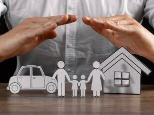 man holding hands over paper house and paper family display in a protective manner